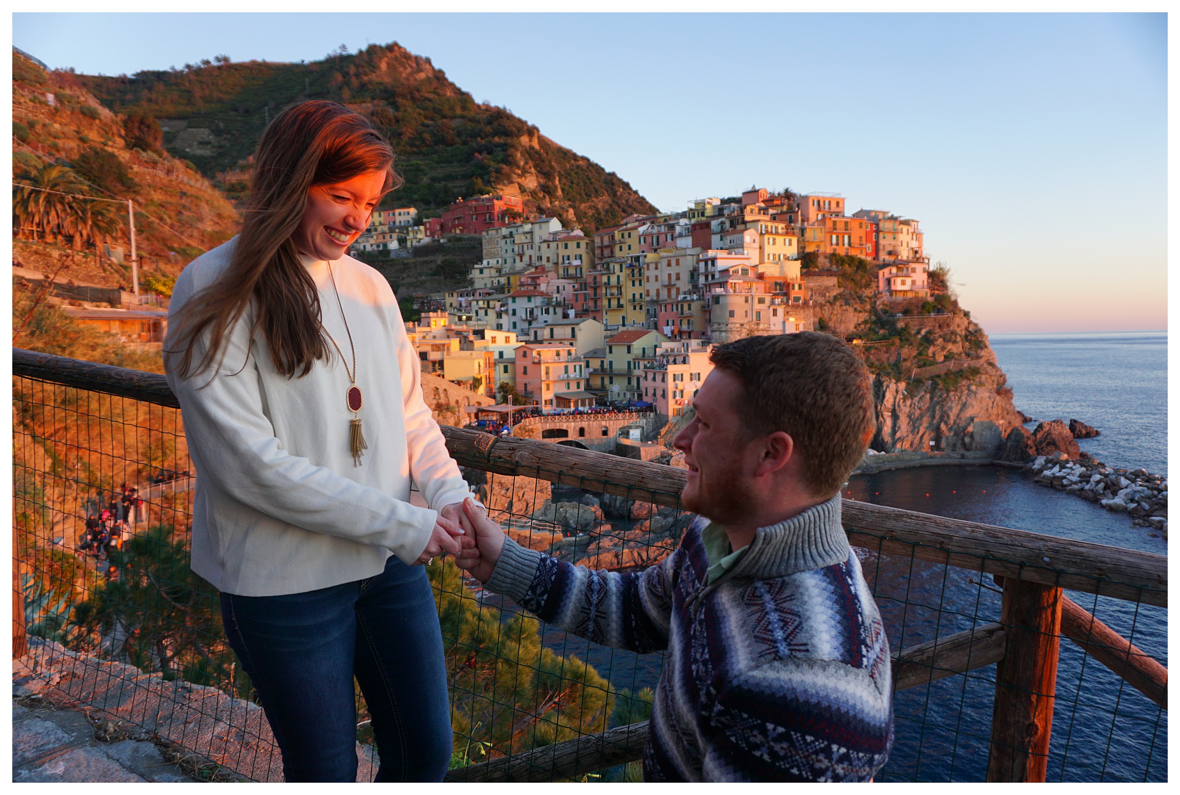 Guy on one knee proposing to girl with a cliffside city called Manarola in the background in Italy